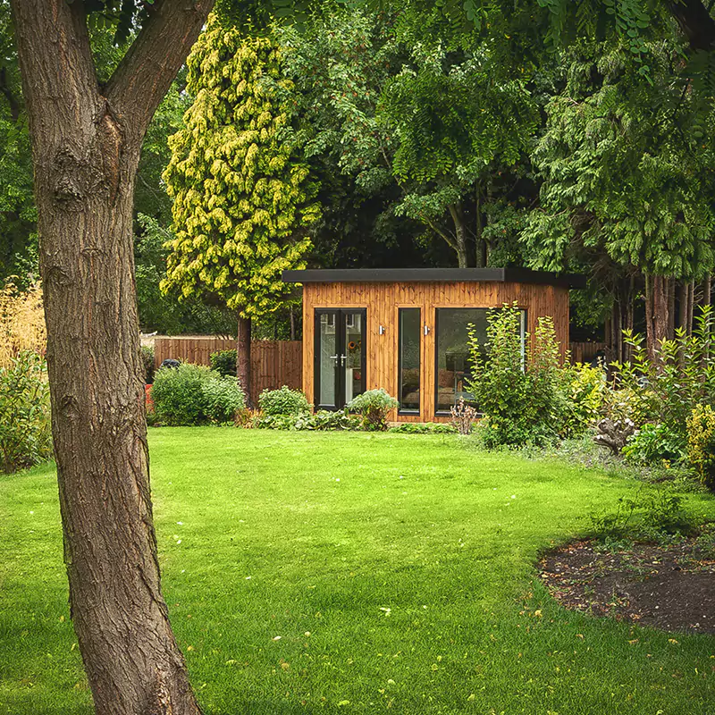 Redwood Garden Room Hobby And Craft Building in grassy lawn area with hedge in front