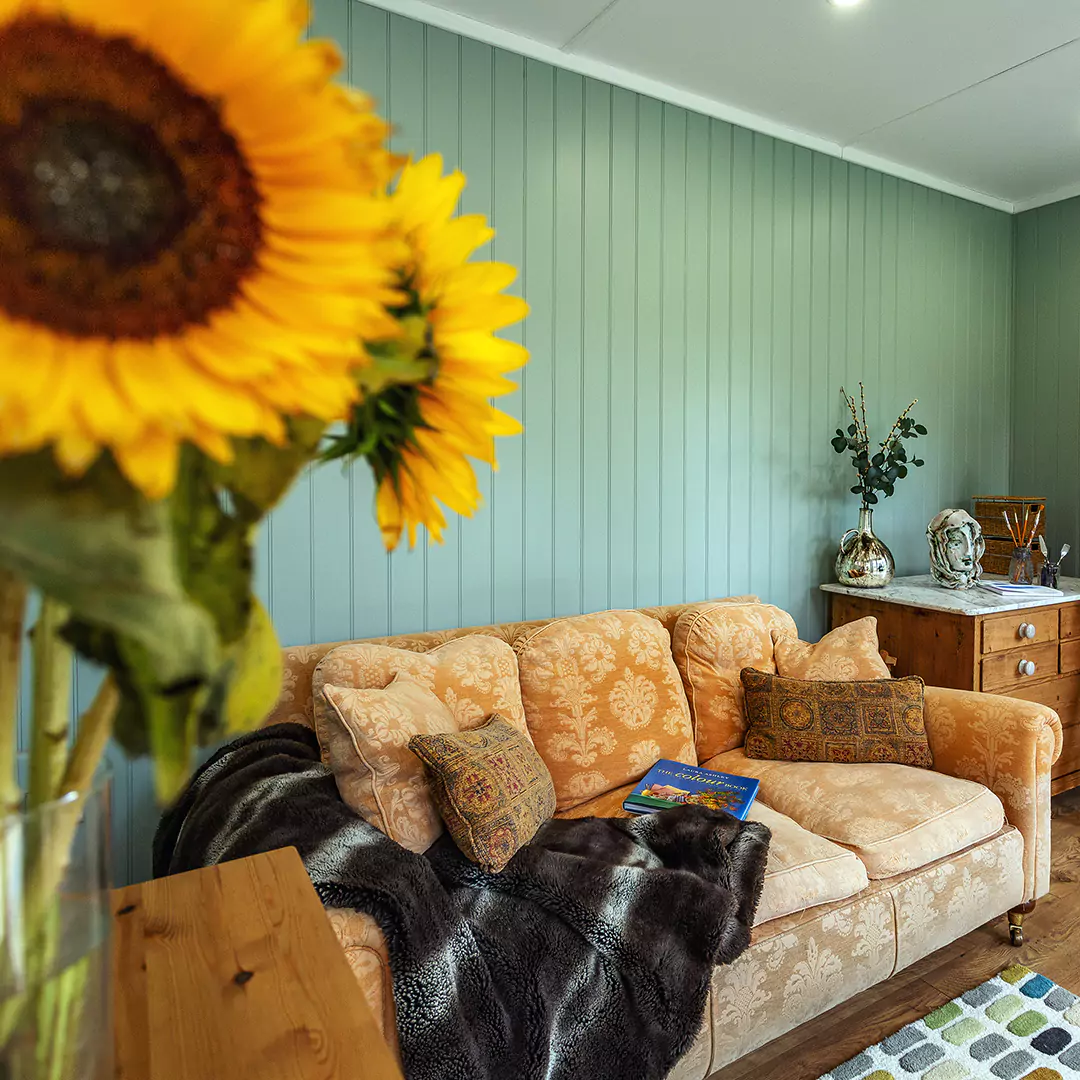 Garden room interior with sage green feature wall and leather sofa with sunflowers