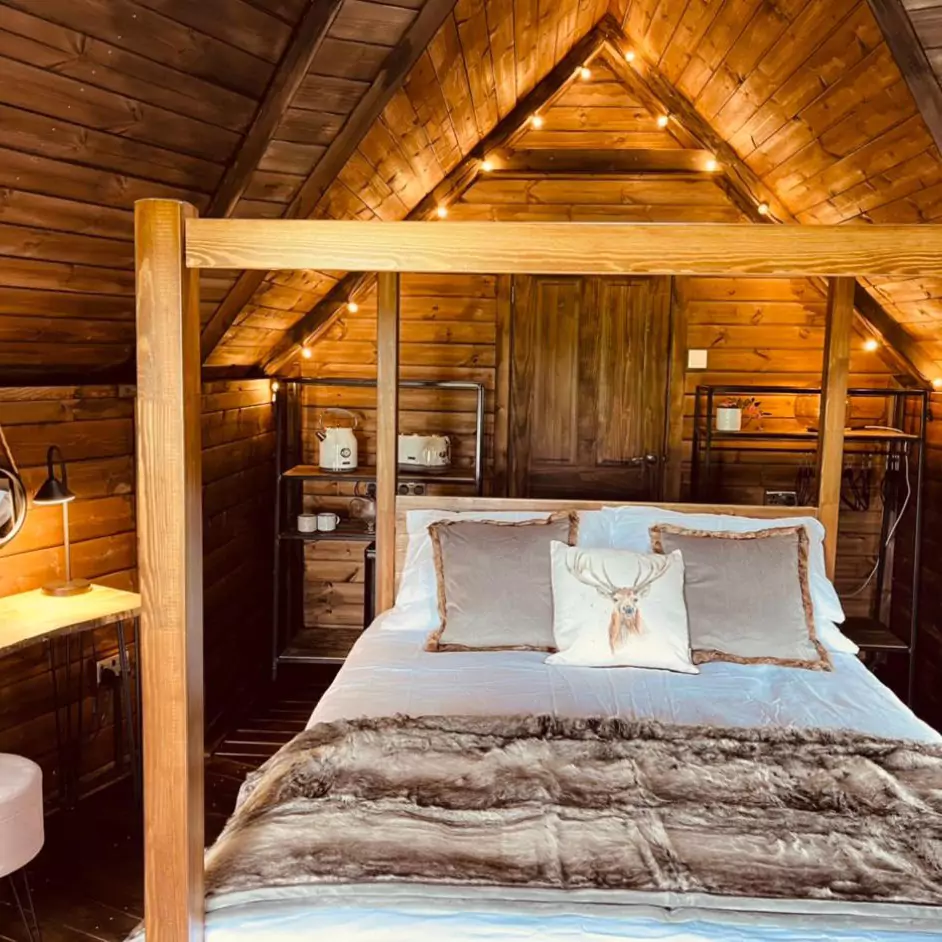 Interior of a luxury timber glamping lodge with four-poster bed and fairy lights