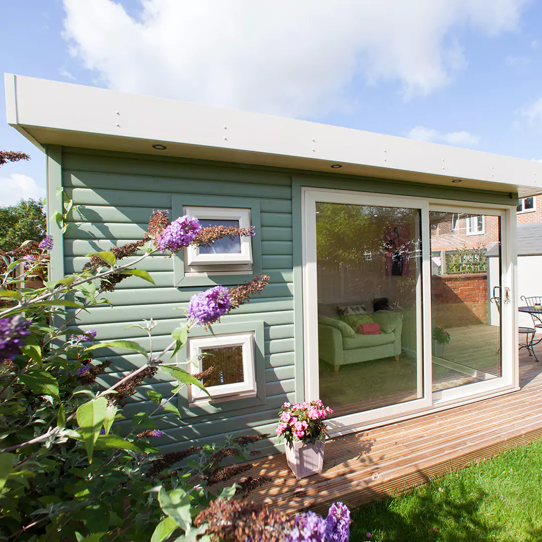 small green redwood garden bar building with a patio area and potted plants with garden furniture