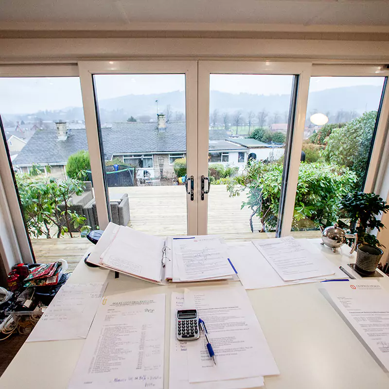A desk inside a home business garden room with papers and a calculator on it