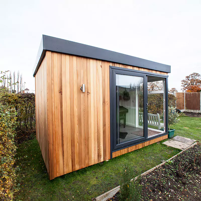 External image of Cabin Master Garden Room with bench in front surrounded by grassy lawn area with potted plant