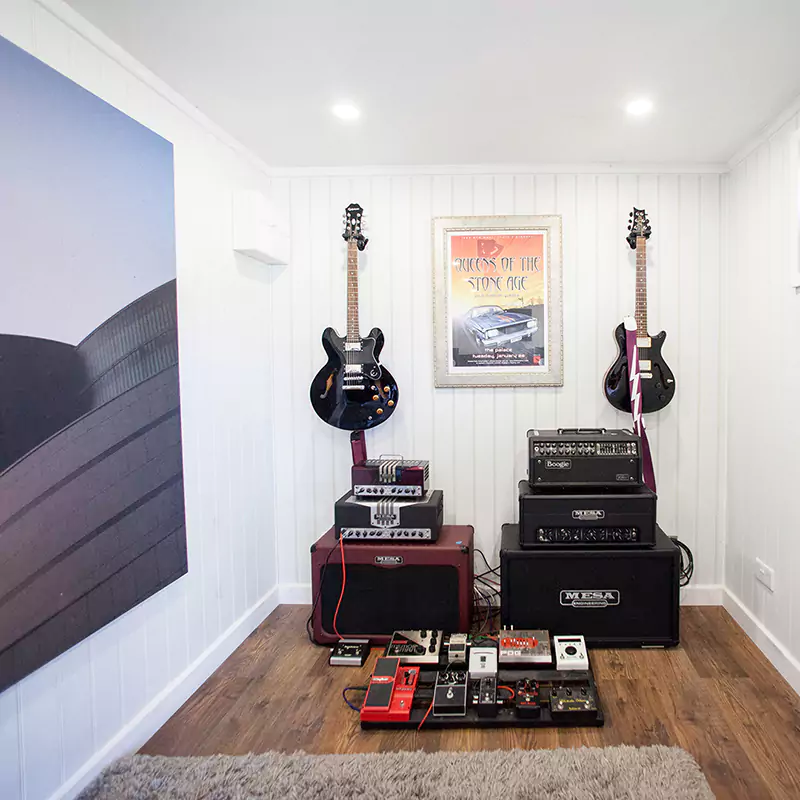 Inside view of Music Room with 2 electric guitars on wall with stereo system and music equipment and brown furry rug in foreground with large wall hanging on side wall