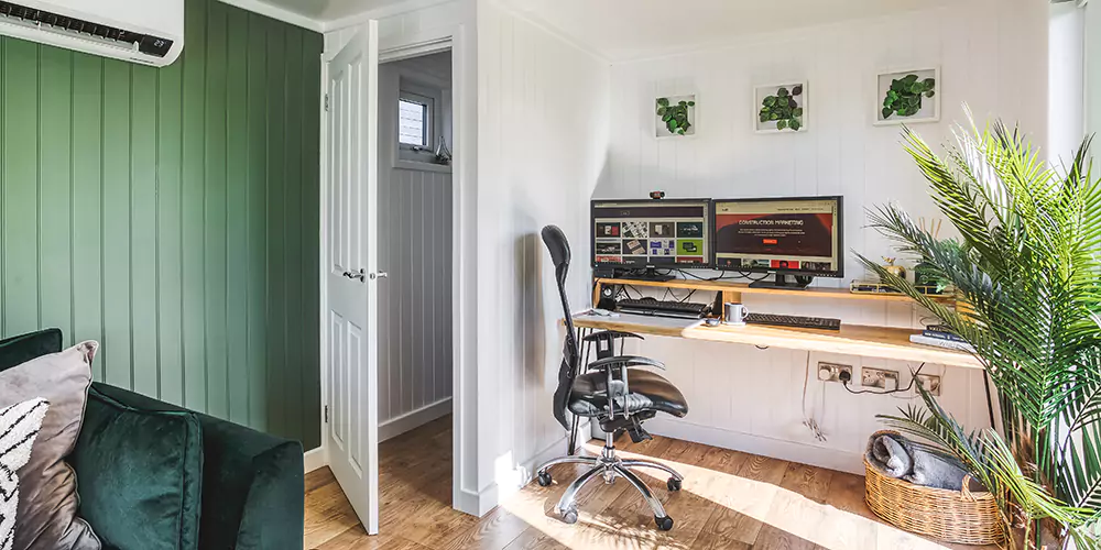 Interior of a garden office with dusky pink desk , laptop ope, candle and reed diffuser 