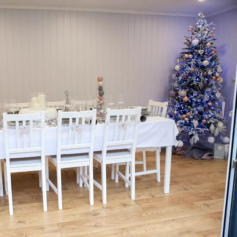 inside view of garden dining room with large glass sliding doors and grey sofa behind large white dining table and chairs with xmas decorations