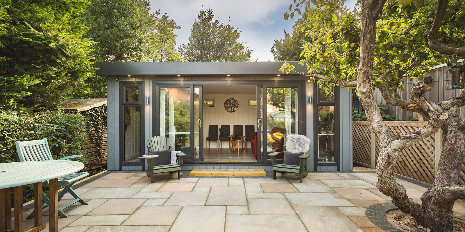External shot of a zero maintenance garden bar with open bifold doors, patio and outdoor seating