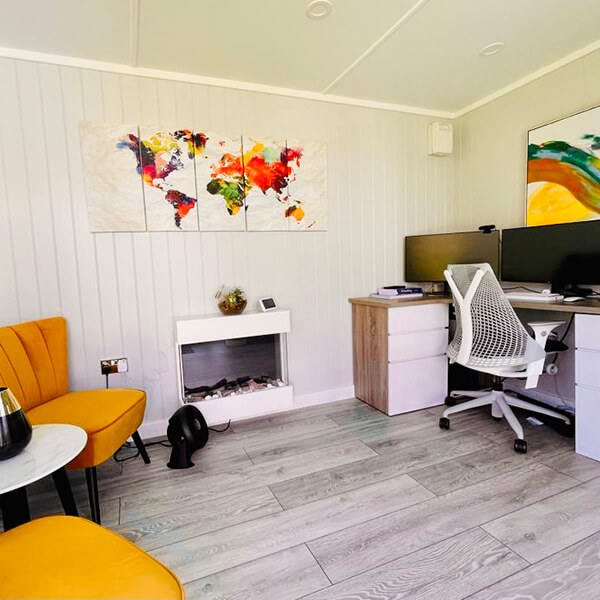 Internal picture of micro office with PC and yellow chairs and wall art and white desk chair and fire place