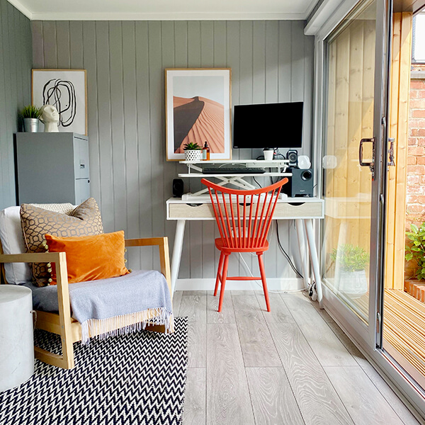 Small Home Office garden building with PC and orange desk chair and corner chair and patterned rug with wall art