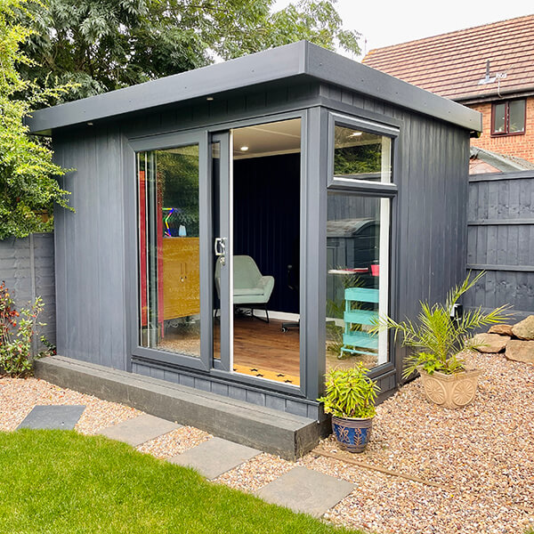 Small Home Office Building Micro Office in garden with potted plants and gravel pathway