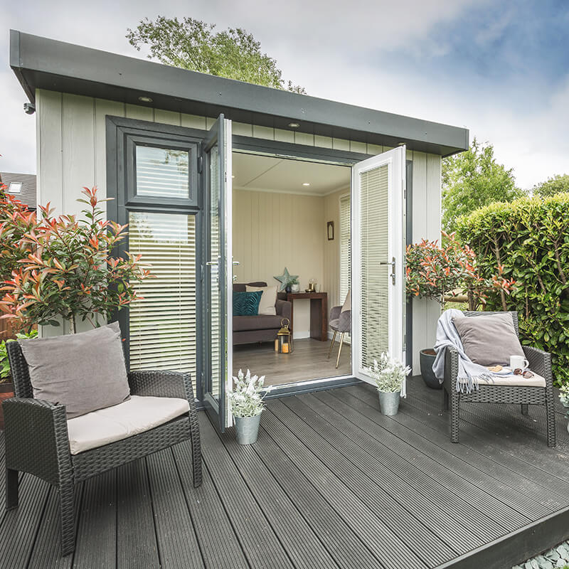 Cabin Master Cedar Summerhouse with doors open onto composite decking with armchairs and view int ogarden room
