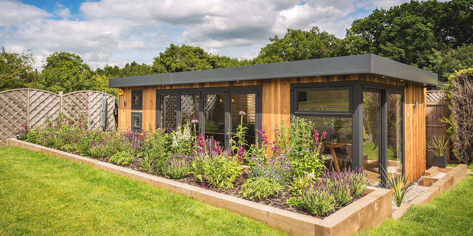 Large timber summer house in garden behind raised flower beds 