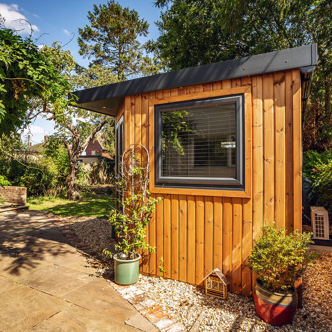 Redwood Small Garden Office Pod Timber Building with roof overhang and patio area with large outdoor plants