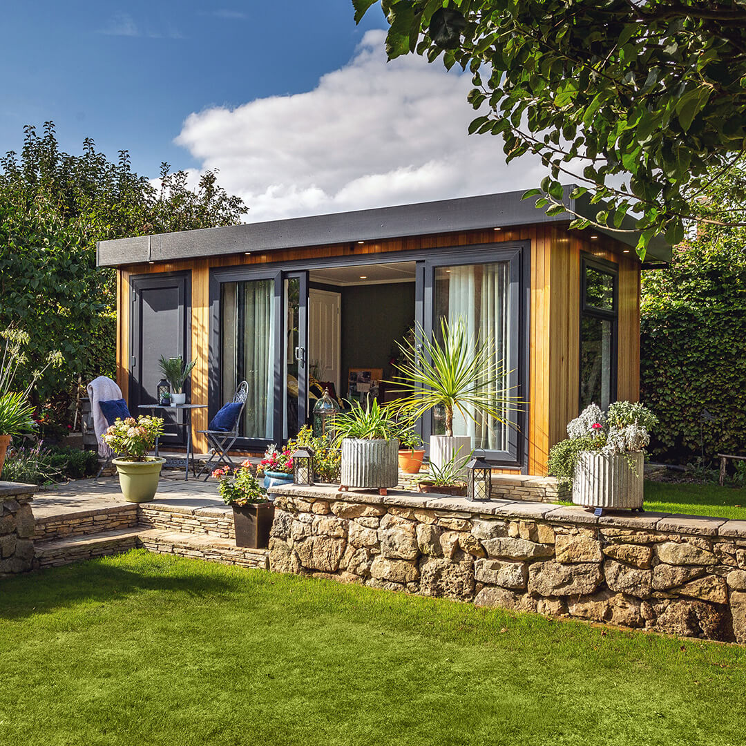 cedar garden office pod with lawn area and patio decking with potted plants 