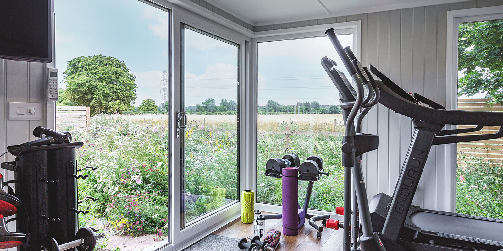 Interior of a garden room gym looking out into a lovely picturesque garden, with gym equipment seen