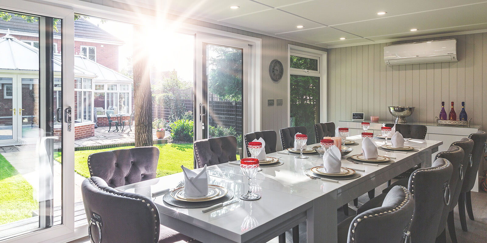 Interior of a garden dining room with contemporary luxury table and chairs, cutlery, crockery and red wine glasses