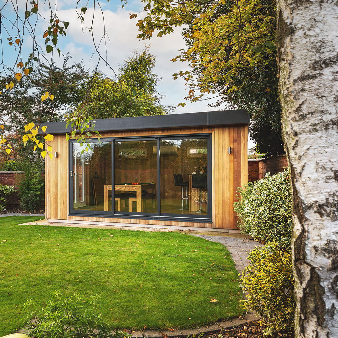 a timber garden building man cave with a patio walkway and large lawn area and large glass doors