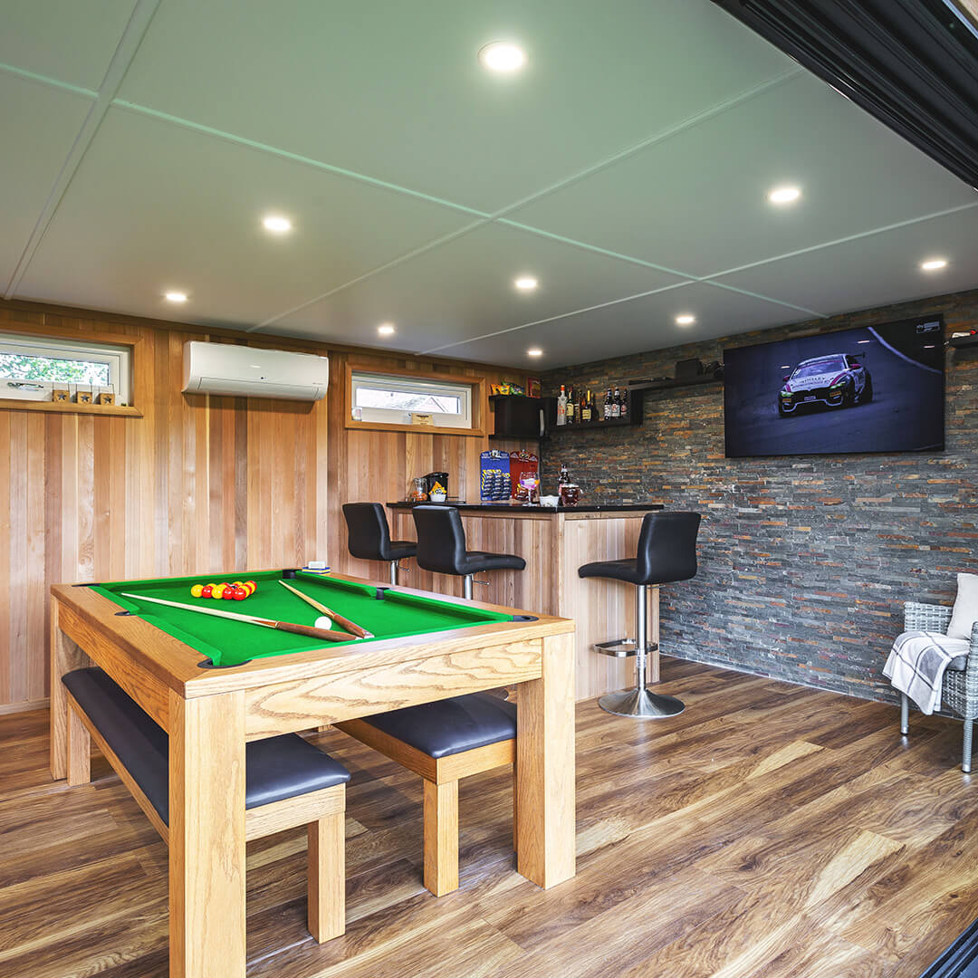 a timber man cave garden building with sliding glass doors and pool table and bar area inside