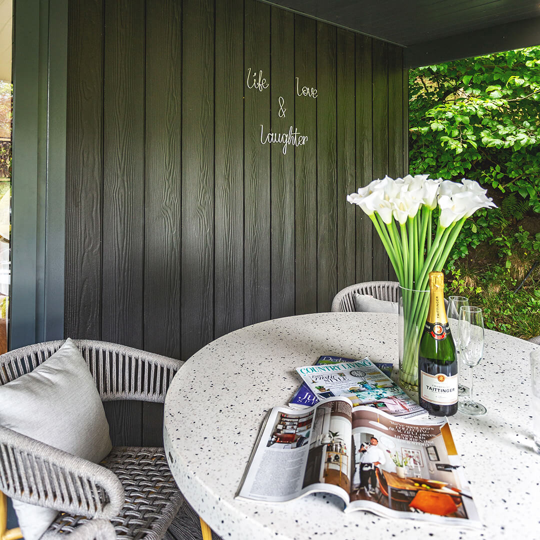 rattan garden furniture with vase of flowers and bottle of prosecco on a table on large veranda garden building