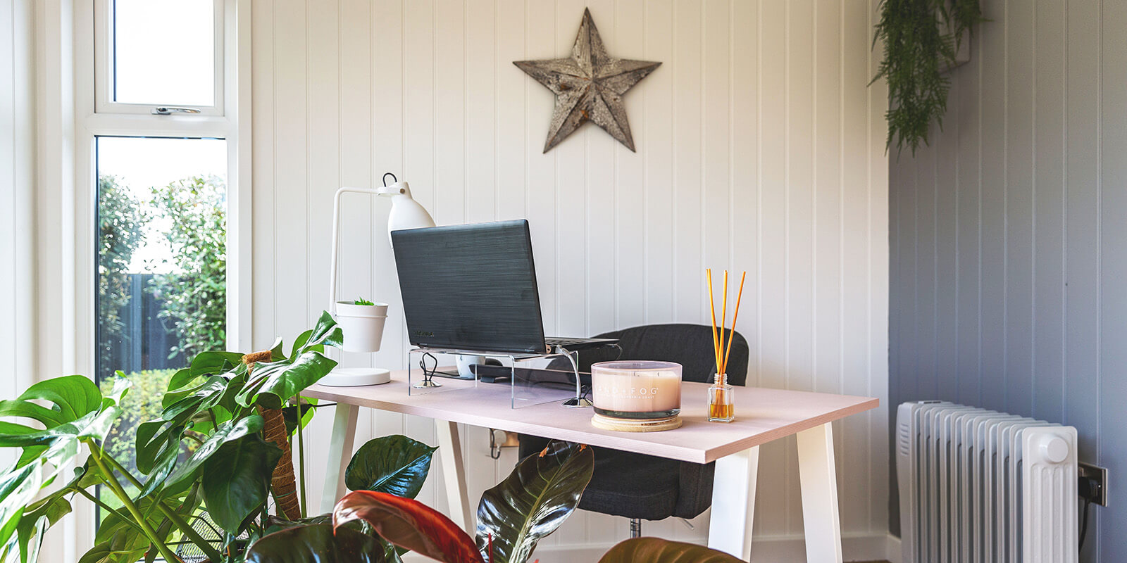 Interior of a garden office with dusky pink desk , laptop ope, candle and reed diffuser