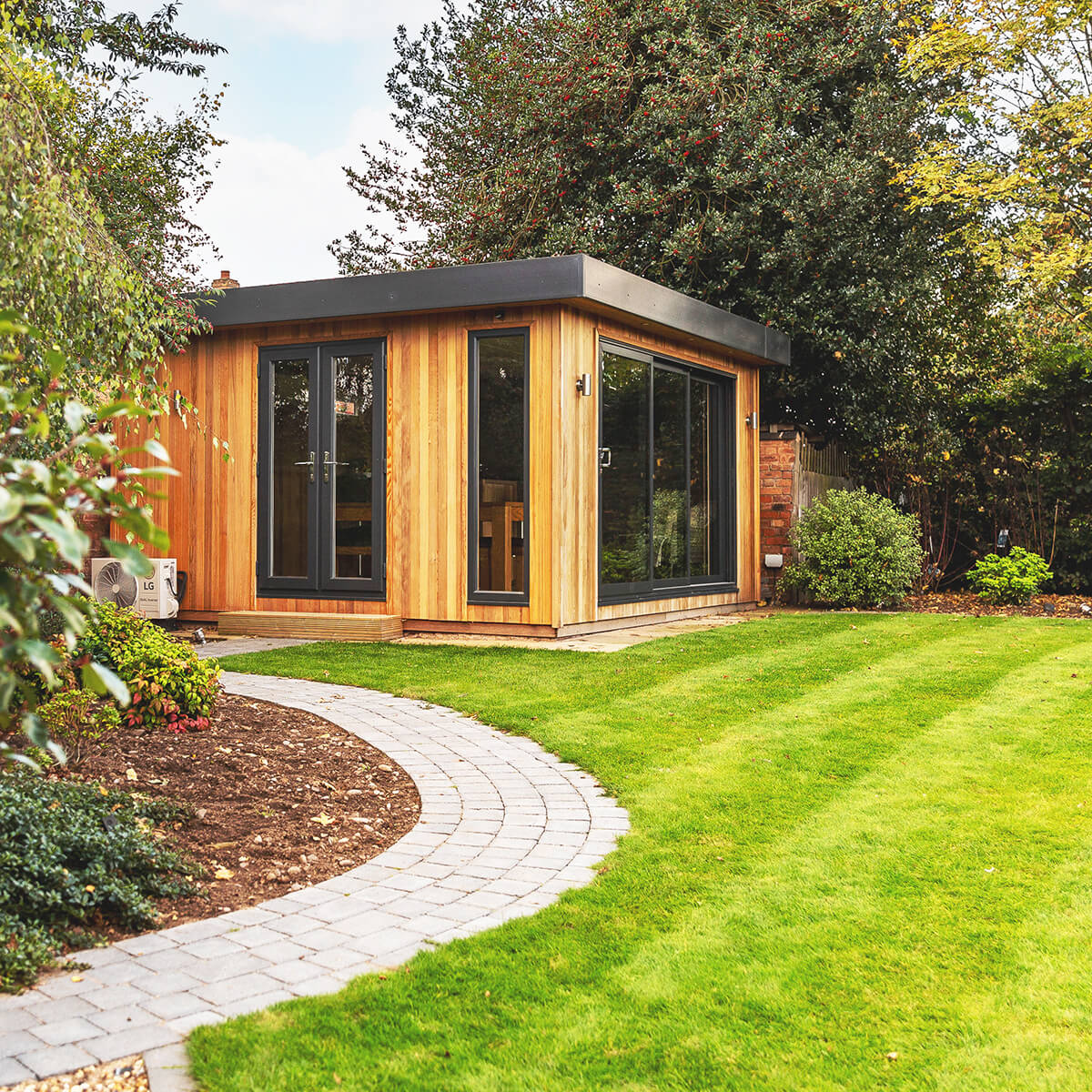 a garden room man cave with a patio path walkway leading to it next to a large lawn area