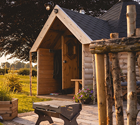 Timber camping cabin for glamping with BBQ and planters outside