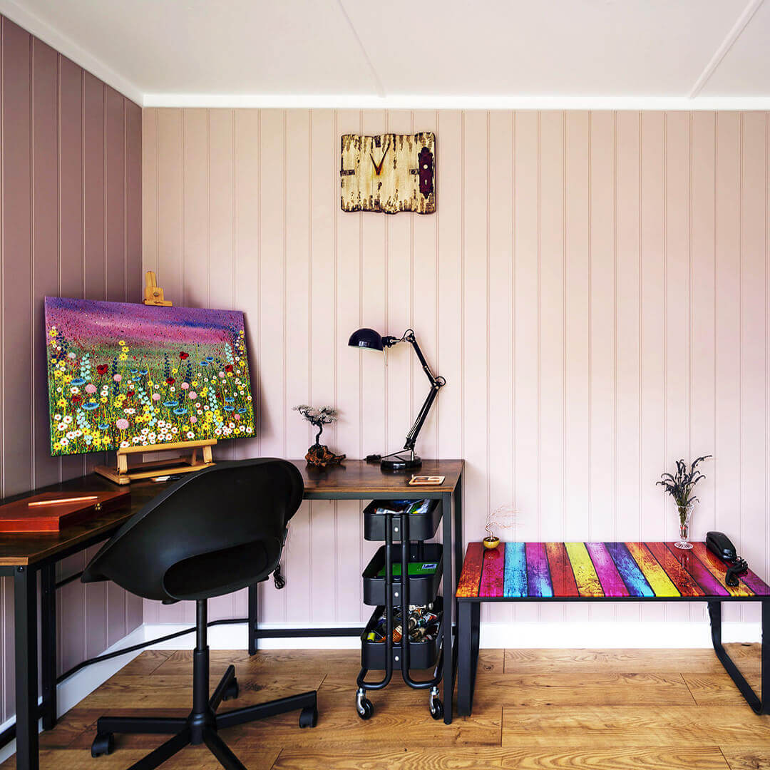 inside view of cabin master garden office building with view of desk and chair and large painting with colourful glass side table