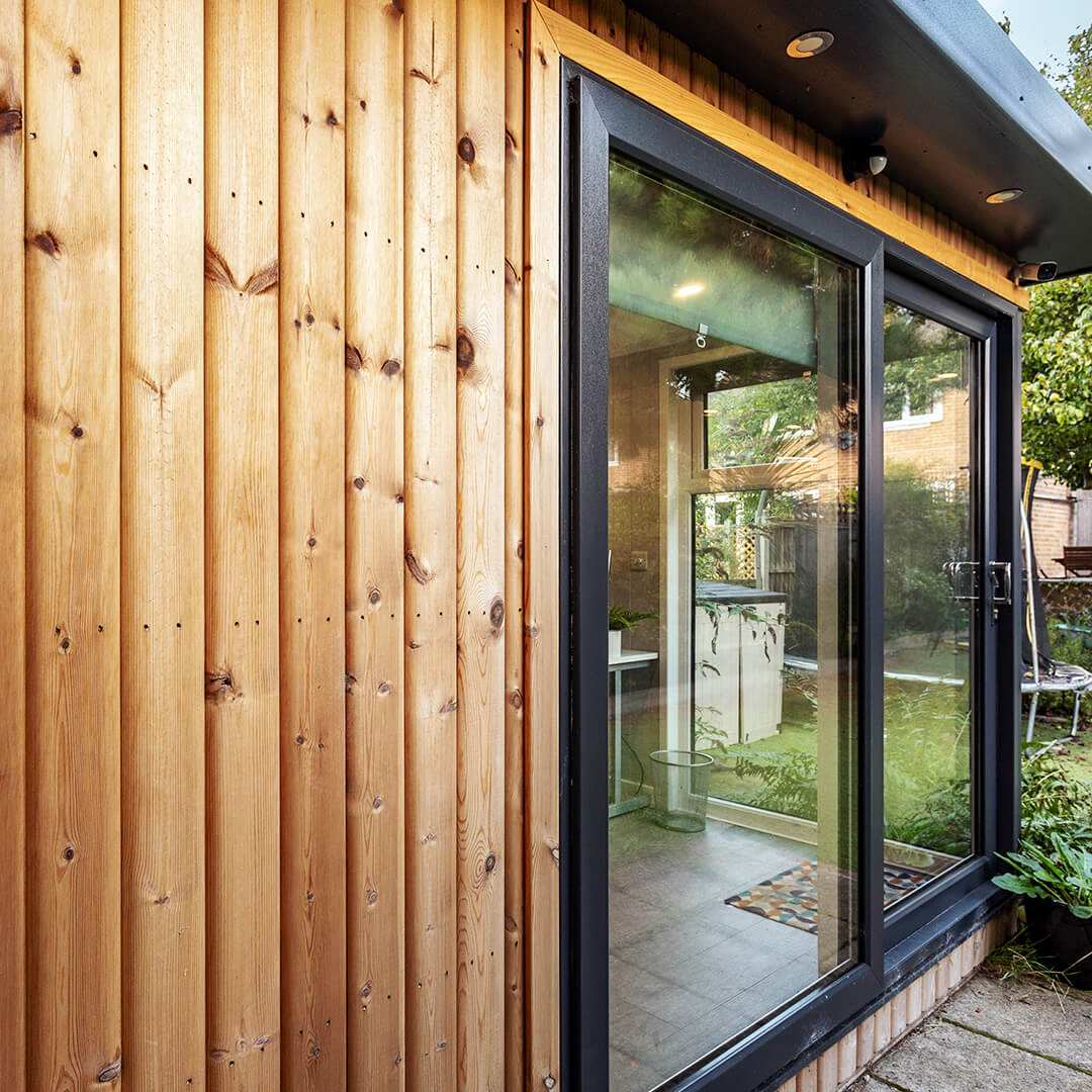 Corner Redwood Garden Office with view of green lawn and  colourful door mat