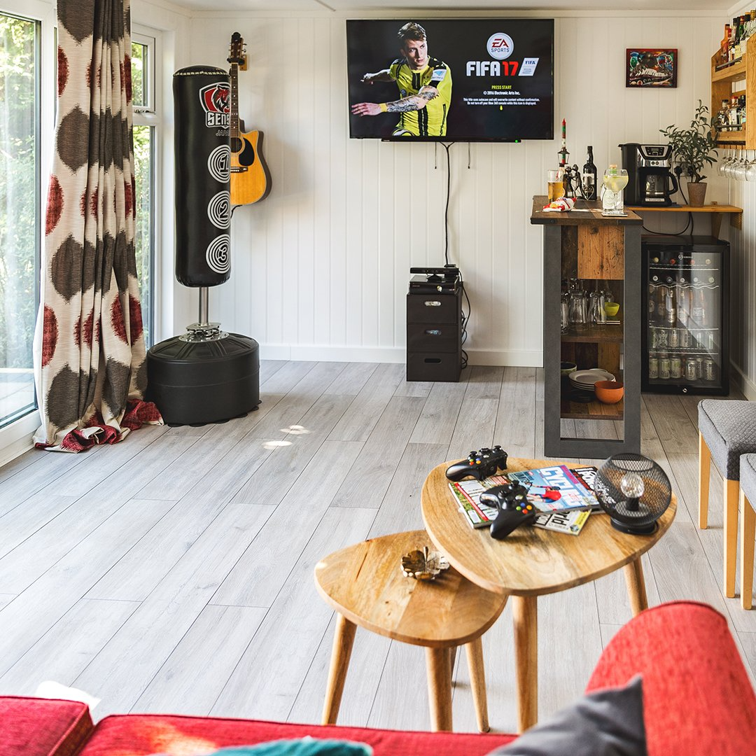 Garden Room with red sofa and small coffee table with gaming console and magazines on top of it and large bar with mini fridge