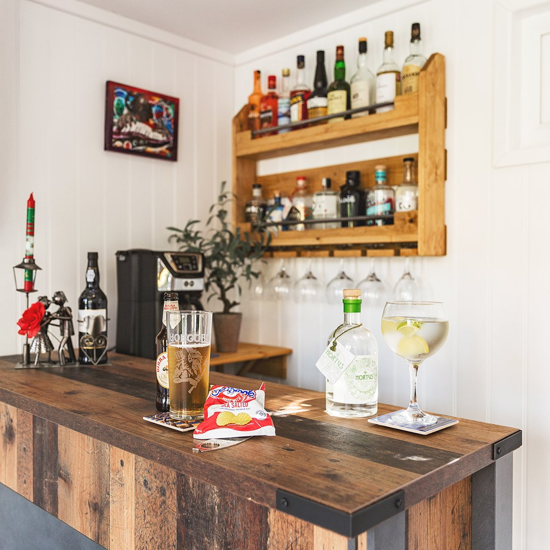 large garden bar with wooden table tops and drinks rack with pint of beer and packet of crisps and glass of gin 