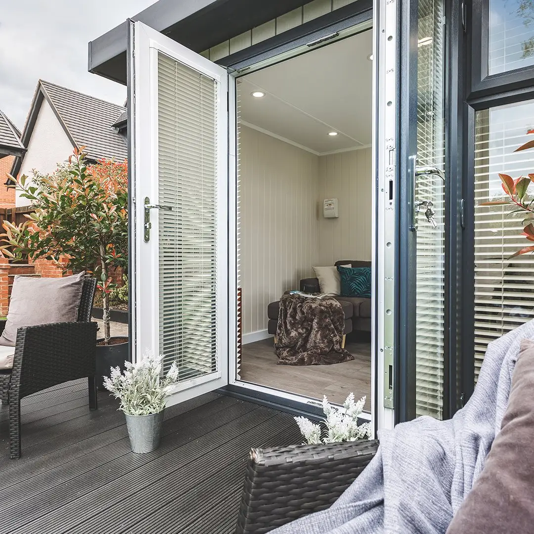 Garden Room with timber decking and outdoor plants and rattan garden furniture with open doors and grey sofa