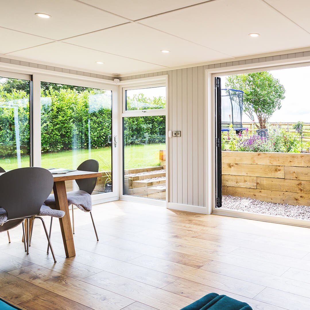 Large garden room with hardwood floors and grey chairs and brown table