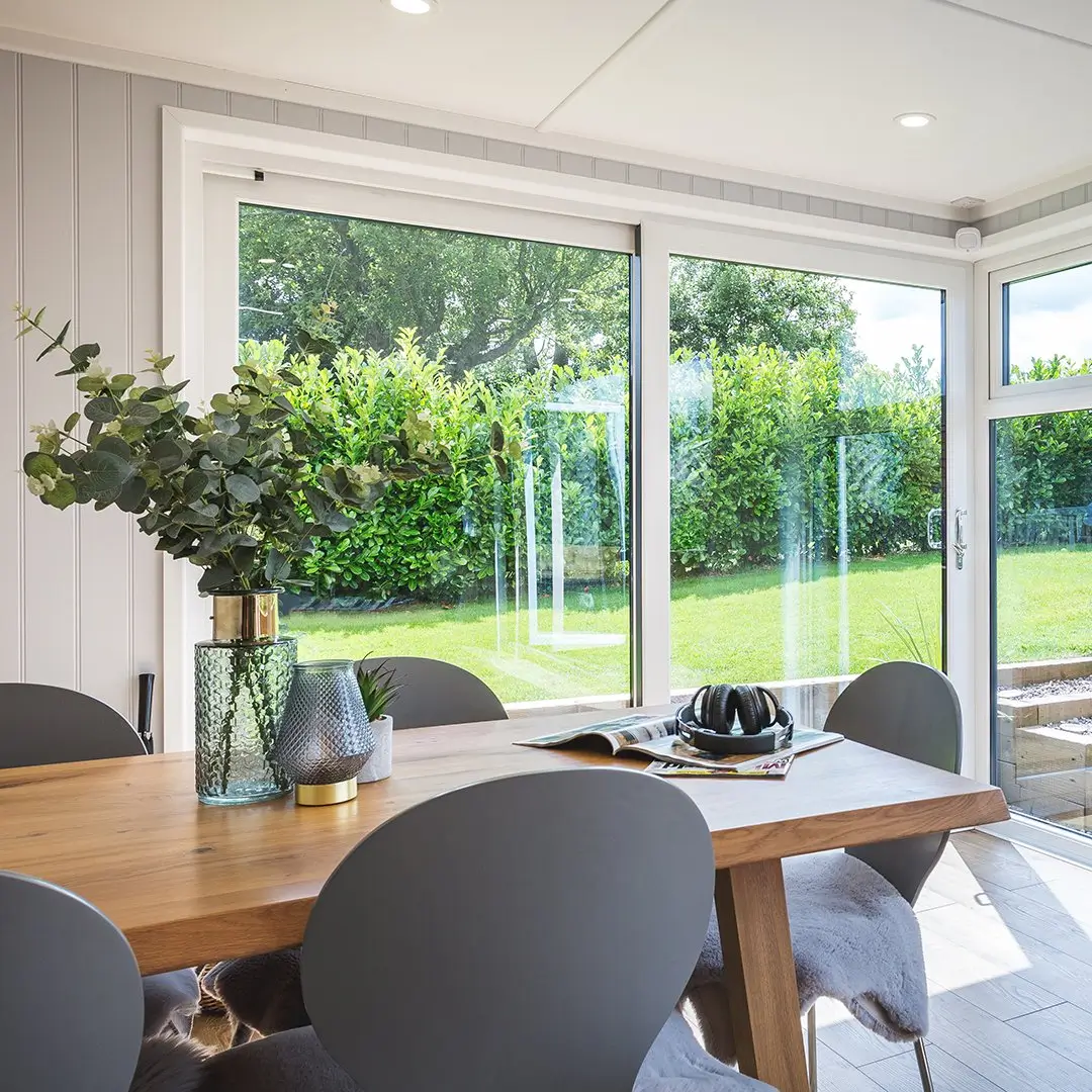 garden room with large glass sliding doors and wooden dining table with grey chairs 