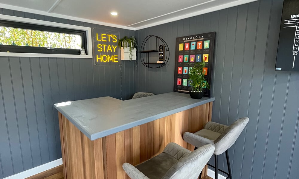Interior of a garden bar man cave with neon sign on wall behind bar with bar stools