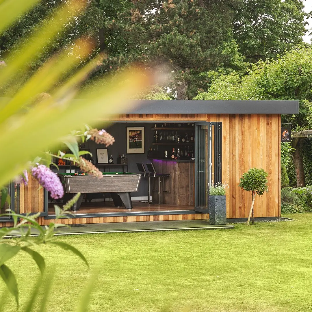 Cabin Master Cedar Mancave in large grassy lawn area with open bifold doors and view of pool table and bar