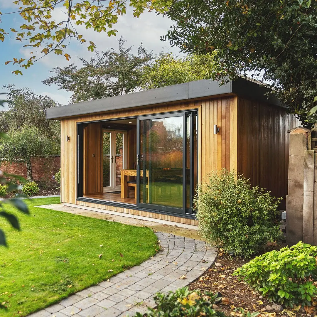 a garden room man cave with a patio path walkway leading to it next to a large lawn area