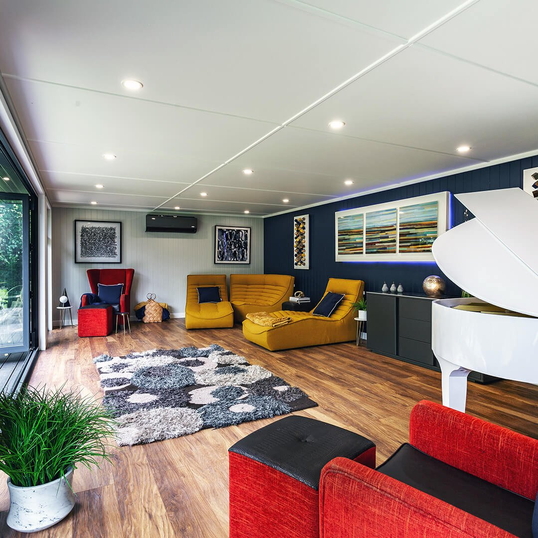 garden room with laminate flooring and tufted black and white rug and red and yellow armchairs and indoor plant and white piano with navy blue feature wall