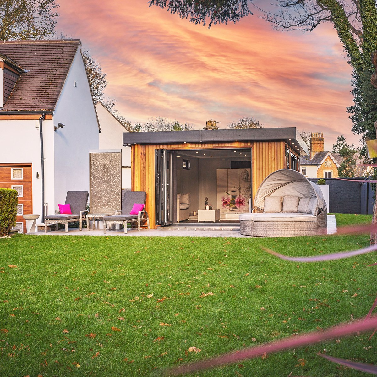 large swim spa garden building with sunset in background and view of large grassy lawn area, there is an array of rattan furniture in front of the building