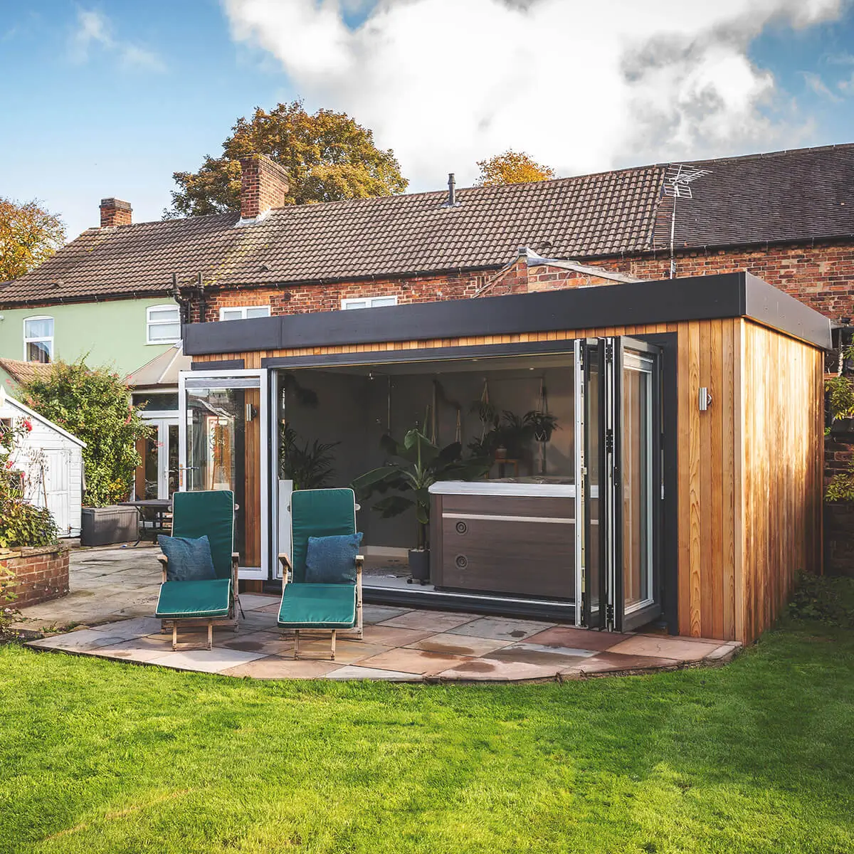 Large cedar outdoor building for hot tub with open bifold doors and sunloungers outside