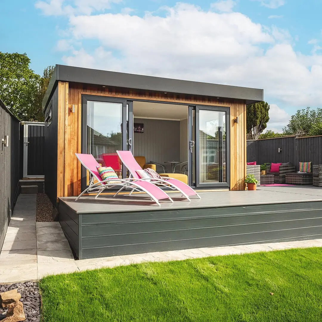 Summerhouse garden room with timber decking and loungers with view of lawn 