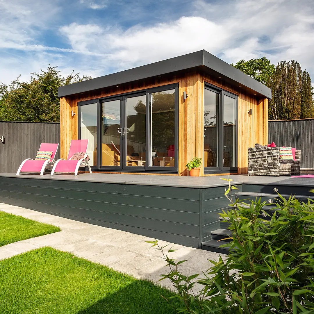 Cabin Master Cedar Garden Room with 2 pink deck chairs in front of it and large timber decking area 