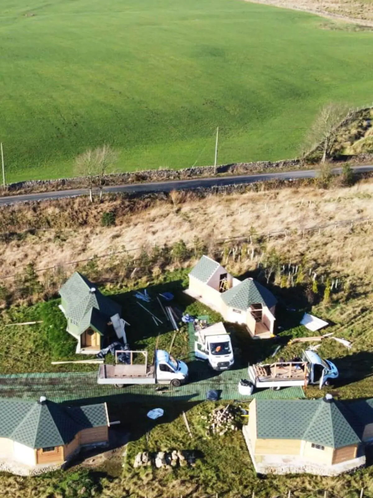 green roofed camping cabins buildings with vans and builders tools in grassy field 