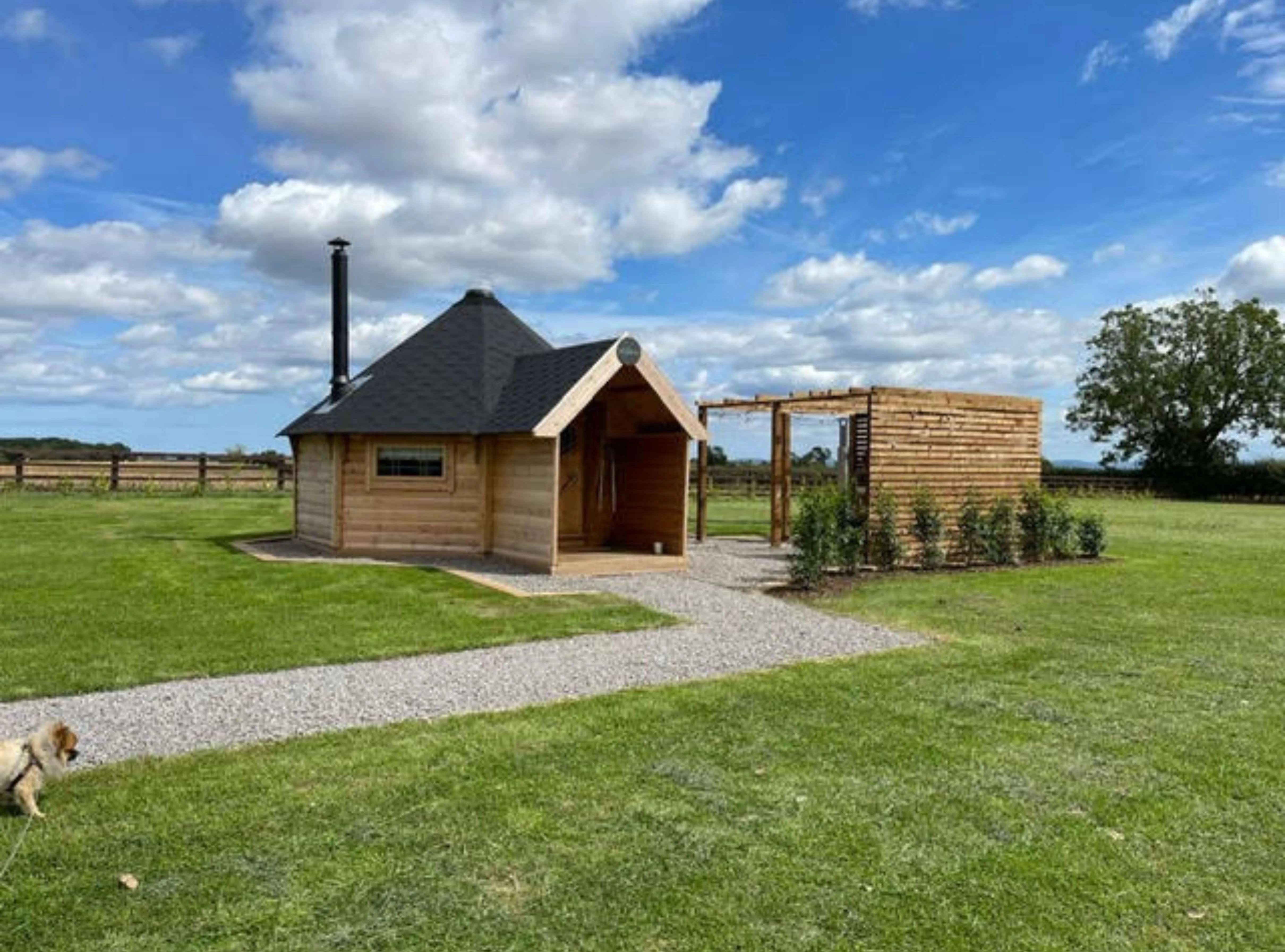 Black roof tiles camping cabin with gravel path and grassy area and pavilion with dog