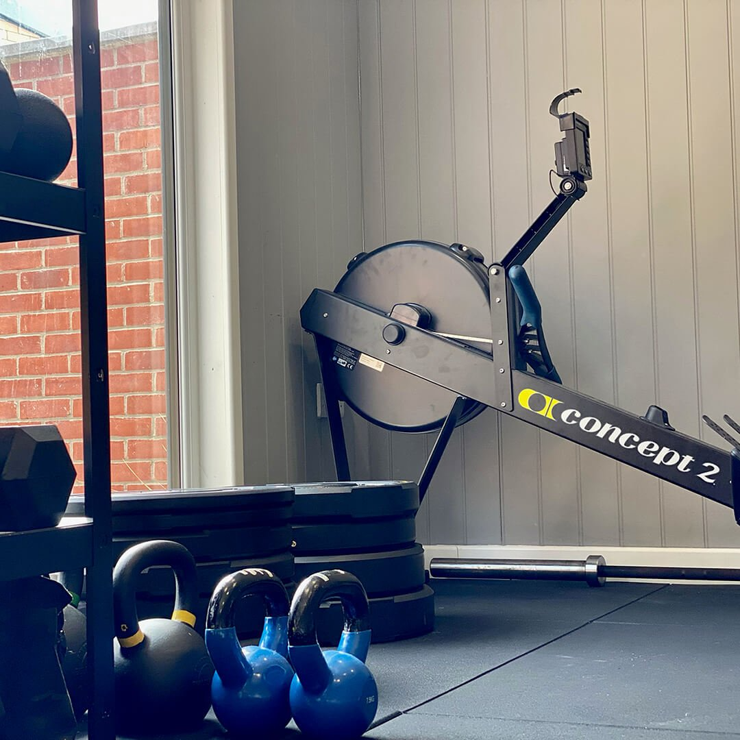 Internal shot of a garden gym room with rowing machine & weights