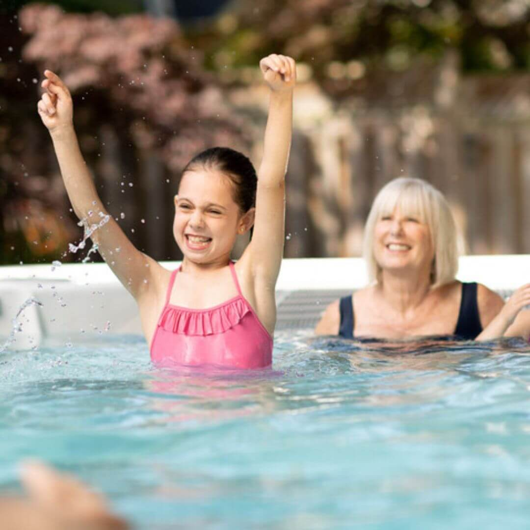 Girl in pink swimsuit and blonde lady in hydropool midlands swim spa playing with water
