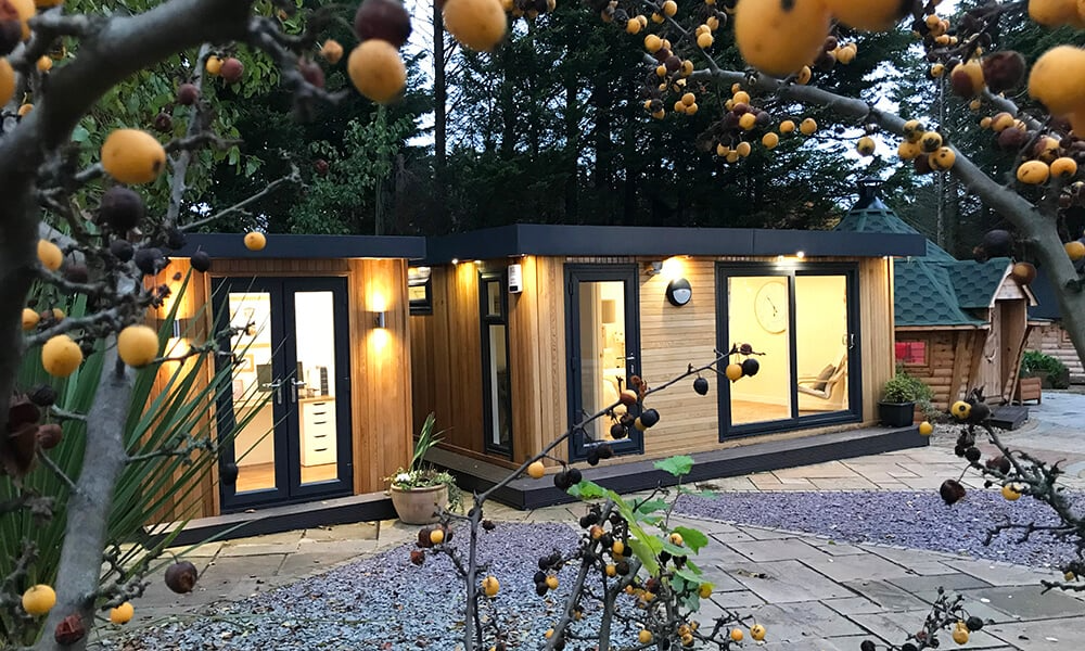 Shot at dusk of the Cabin Master garden room show site with tree in foreground with orange berries