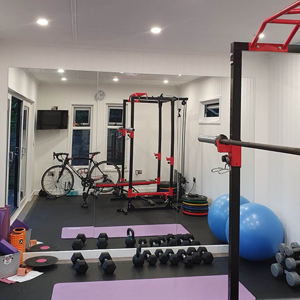 inside view of garden gym with squat rack and bench press and exercise equipment and large mat area with dumb bells 
