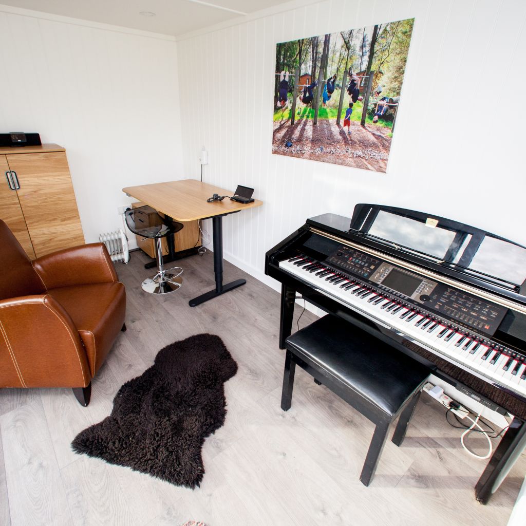 internal view of garden music room with piano and leather armchair and desk in the corner with wall art