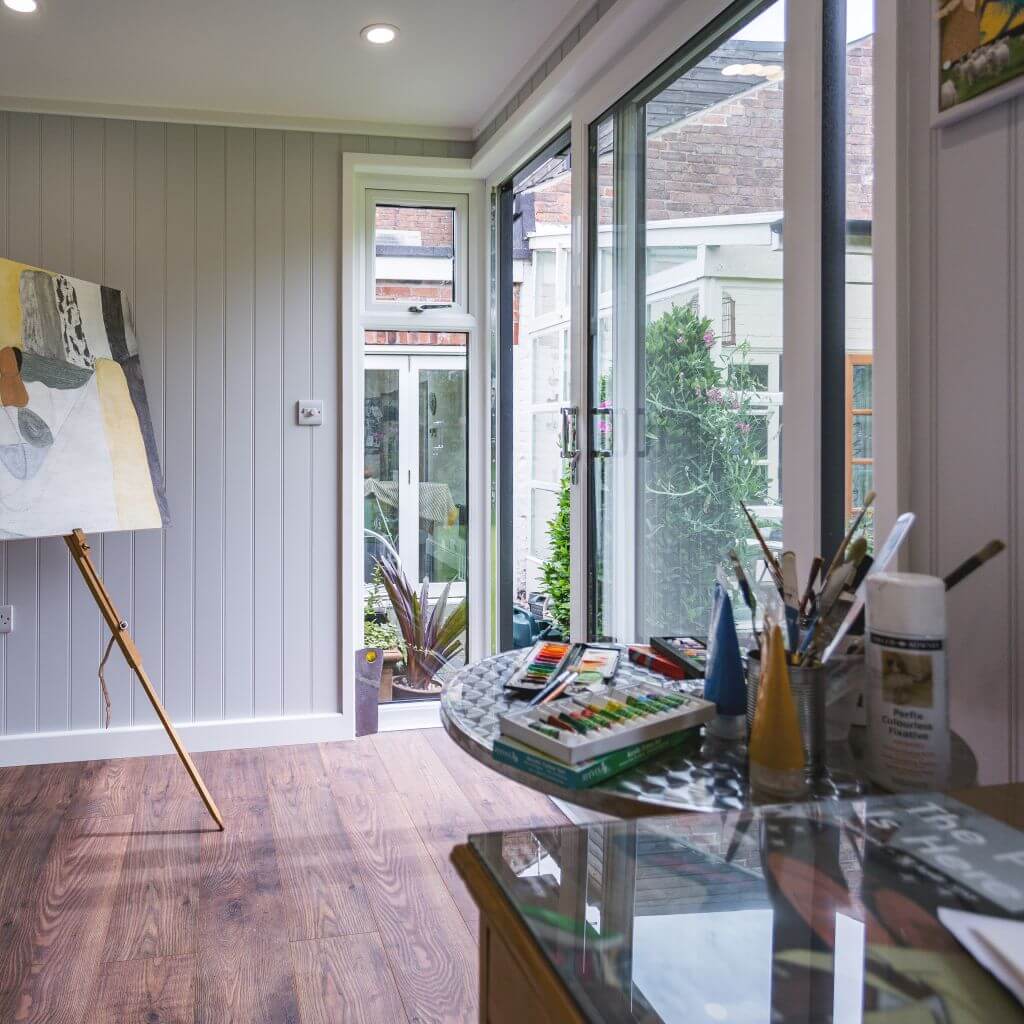 inside view of artist's studio with large easel and paint supplies with large windows and doors