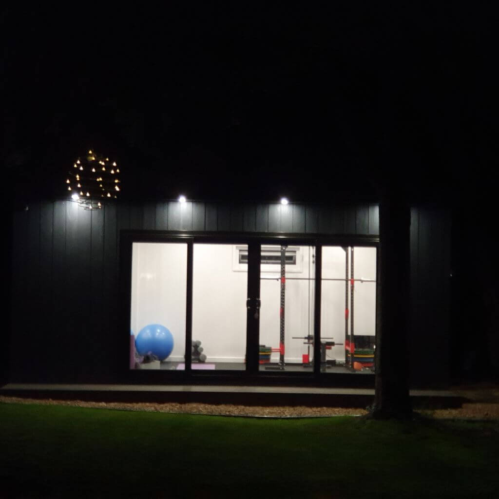 Cabin Master garden gym marley board with spot lights and roof overhang in garden area with squat rack and bench press and exercise equipment