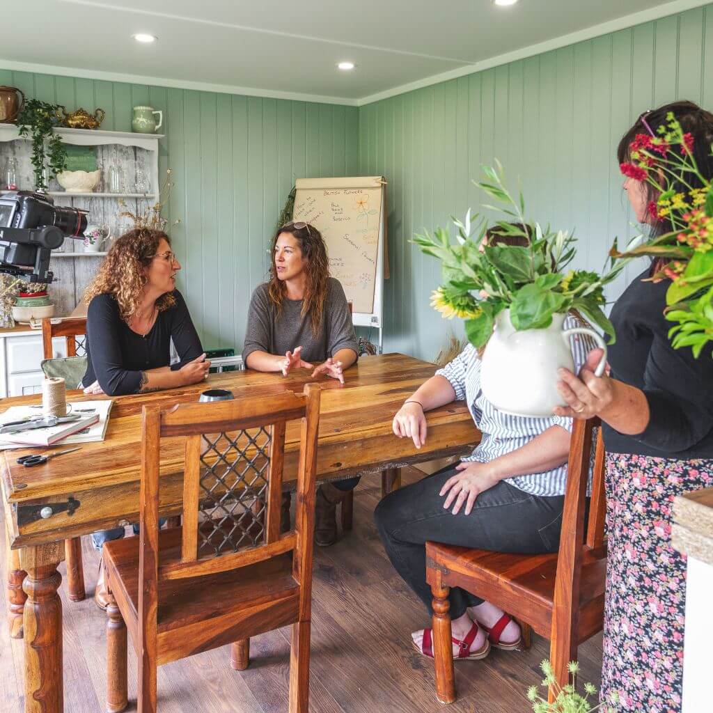 women gathered around a table inside a large home business garden room partaking in a floristry workshop